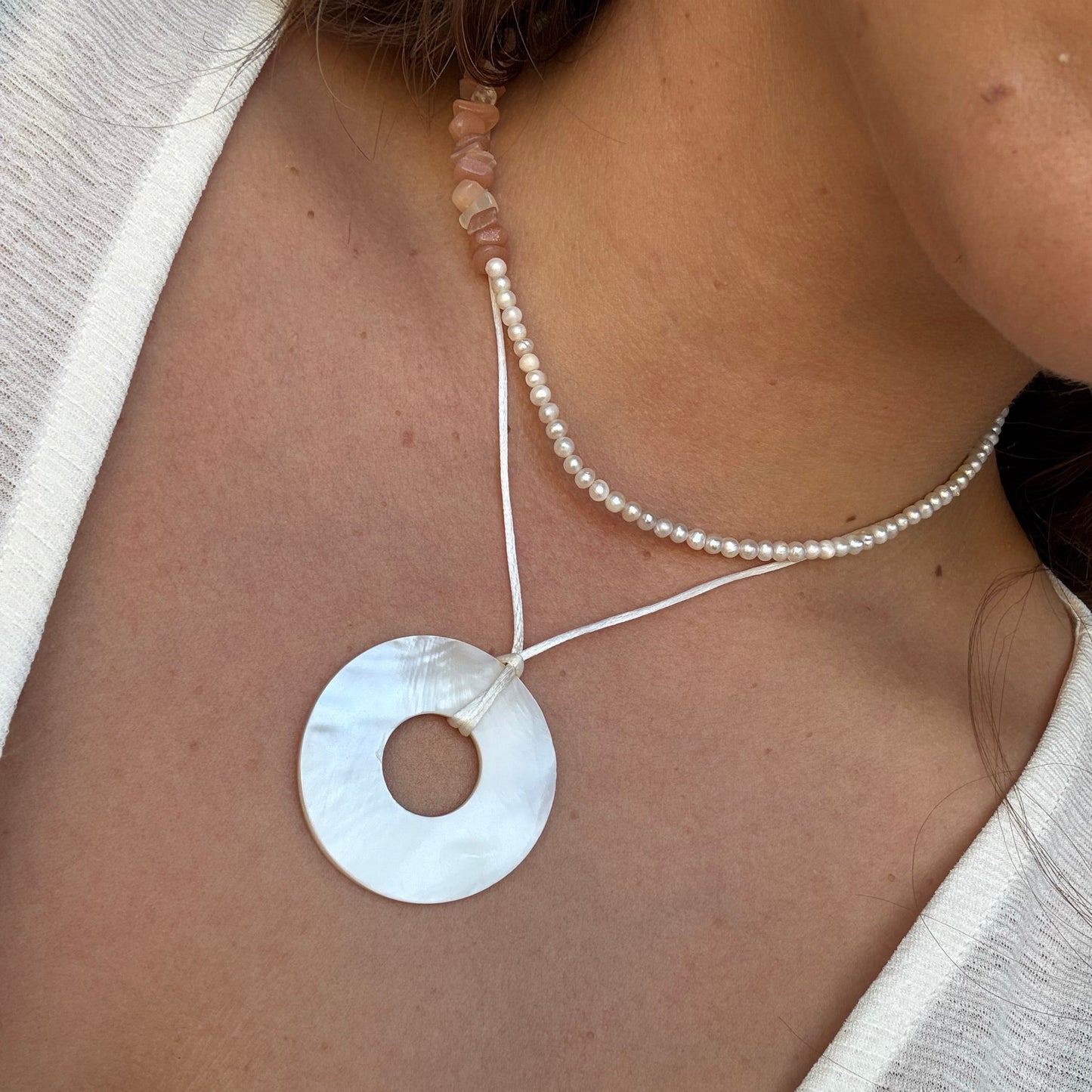 Perlmutt Kreisanhänger als Halskette getragen. Minimalistisch, femininer Schmuck in warmen Licht.
